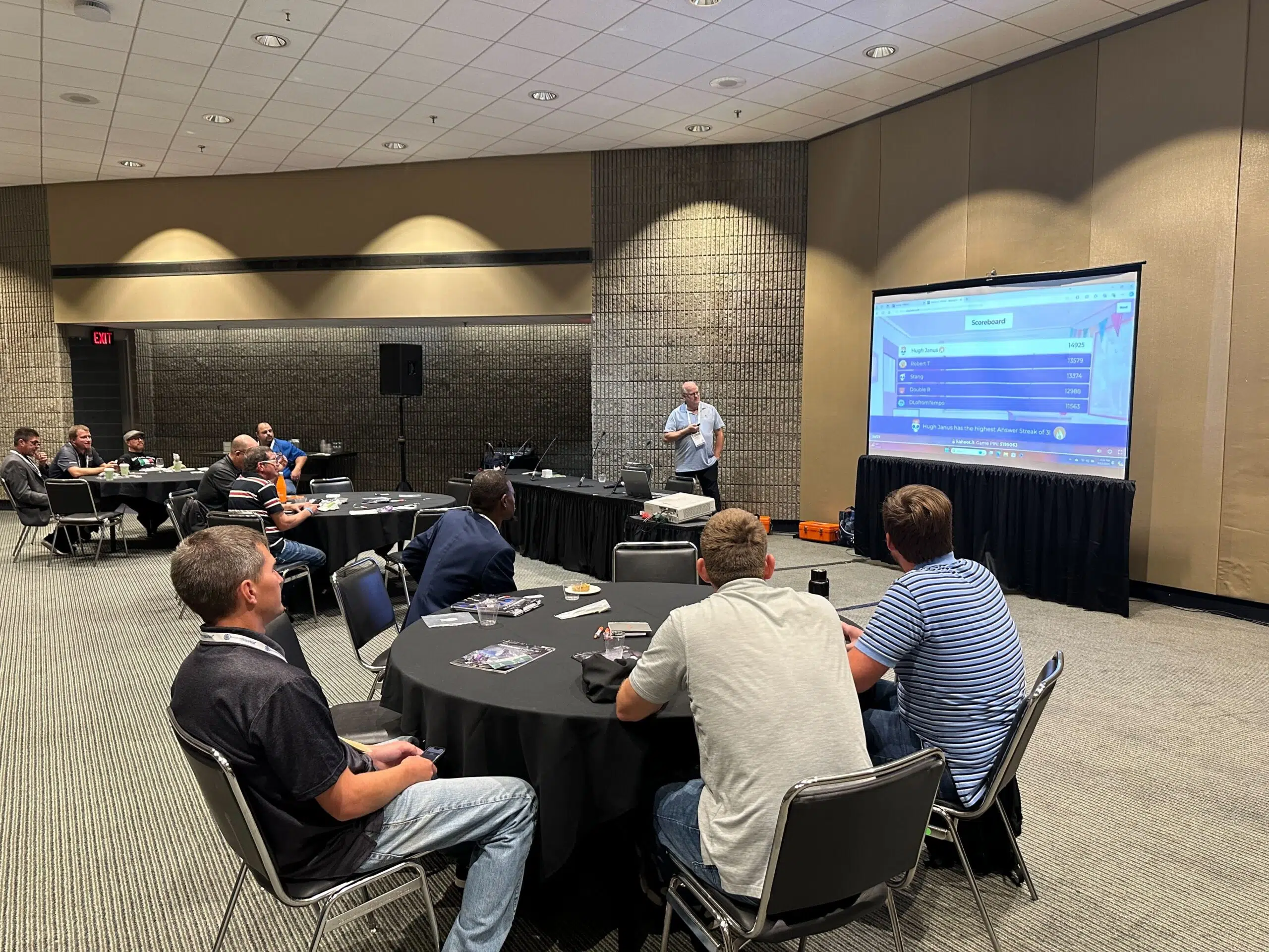 Groups of people at round tables looking at a large presentation screen